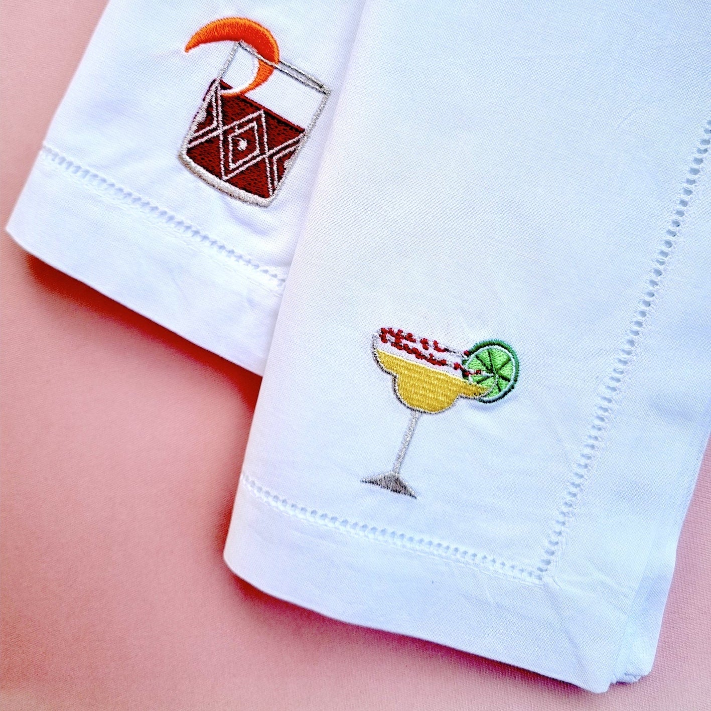 White napkins with embroidered negroni and margarita cocktails on them