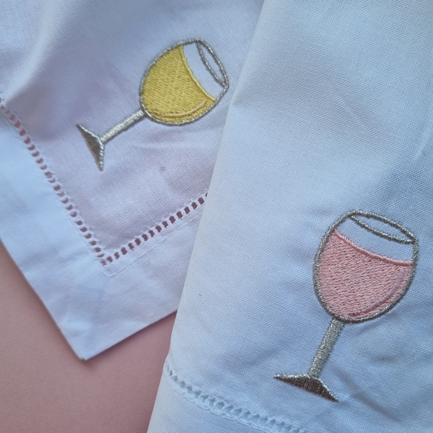 White napkins with embroidered wine glass designs on a pink surface