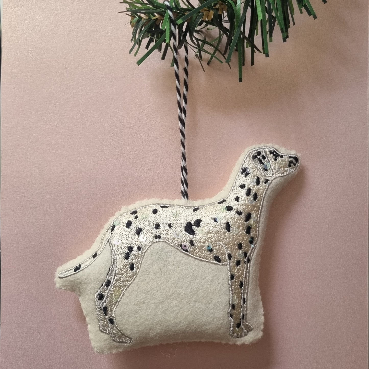A dalmatian embroidered ornament on a pink background with a christmas tree branch