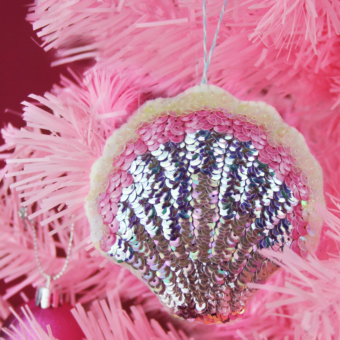 A sequinned scallop ornament on a pink Christmas tree