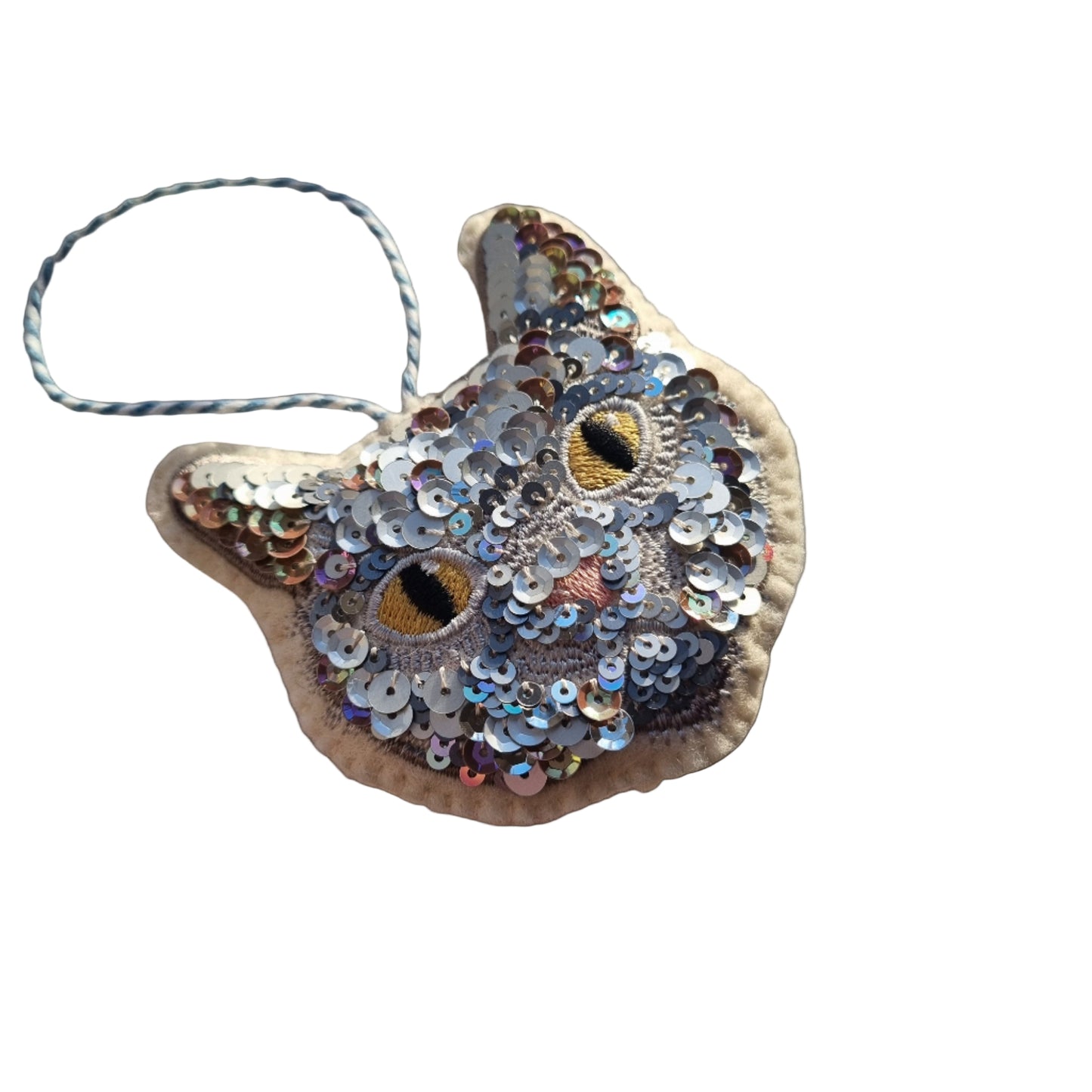 Decorative cat ornament with sequins on a light fabric background