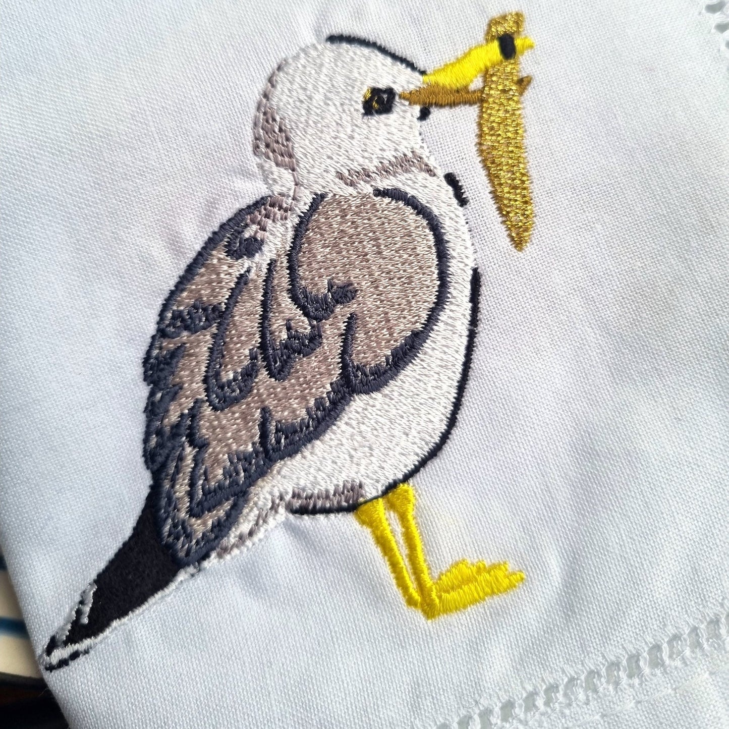 Embroidered seagull with a chip in its mouth on a white napkin