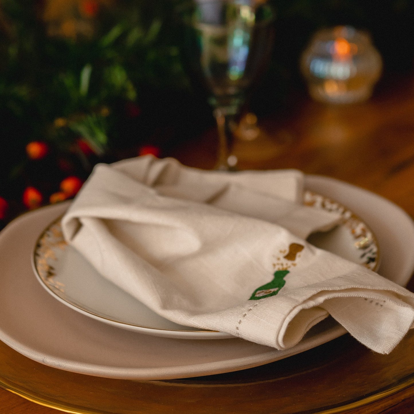 An embroidered champagne bottle napkin on a stack of gold and white plates