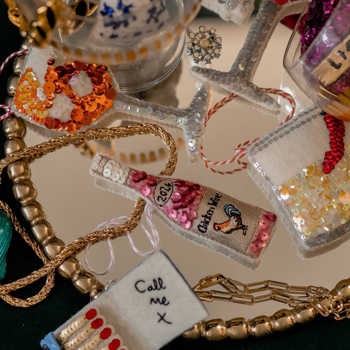 A collection of sequinned ornaments on a mirror with a chicken wine ornament at the centre