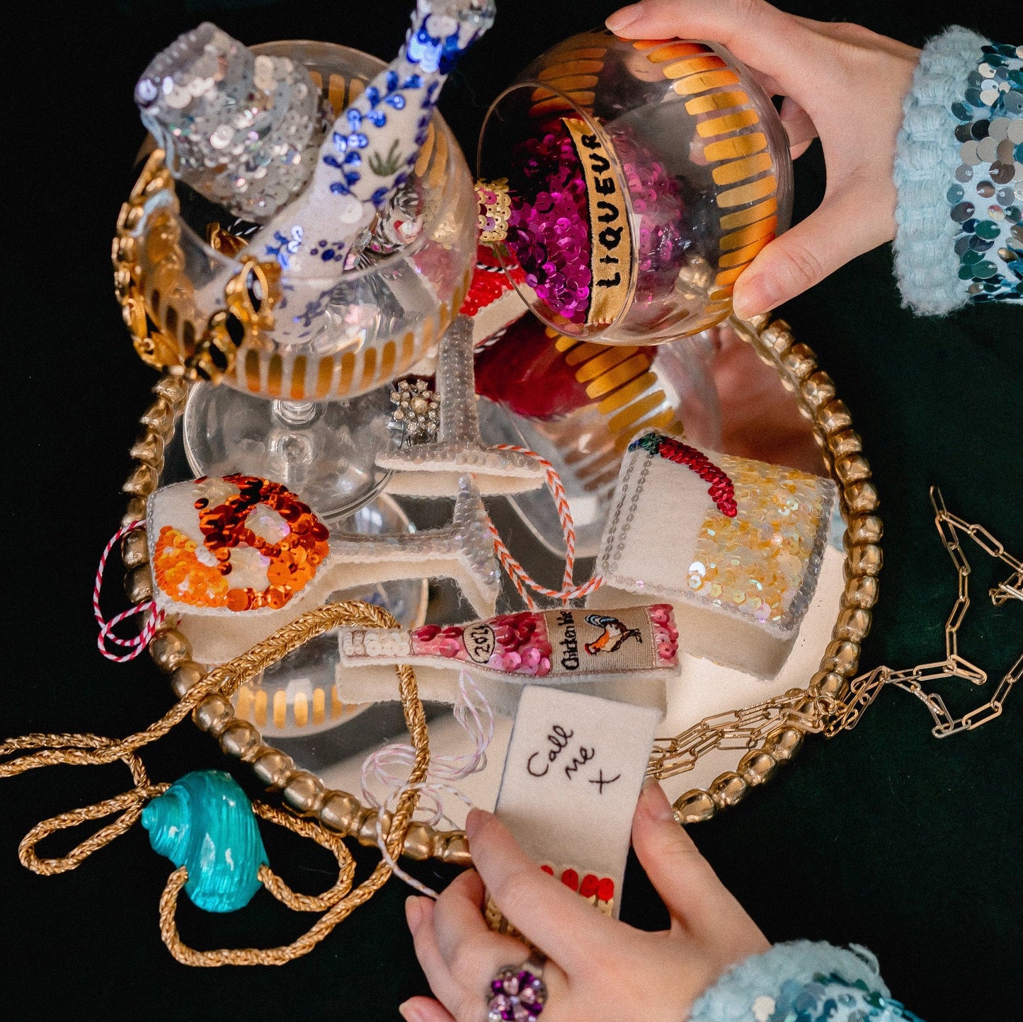 A collection of sequinned ornaments on a mirror with a woman's hands holding them
