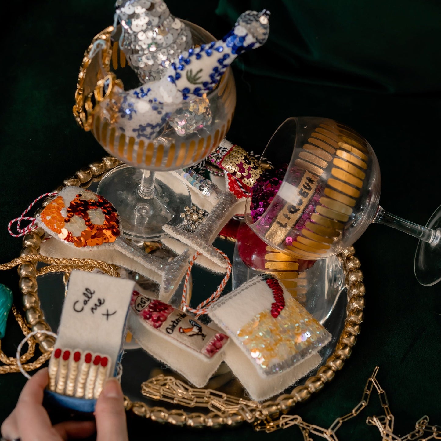 A woman's hand holds an open matchbook ornament on a background of sequinned cocktails on a mirror