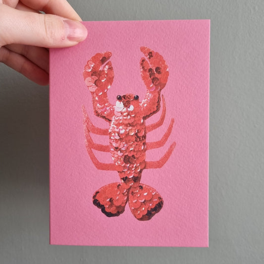 Kate's hand holding a bright pink card with the image of a sequinned red lobster