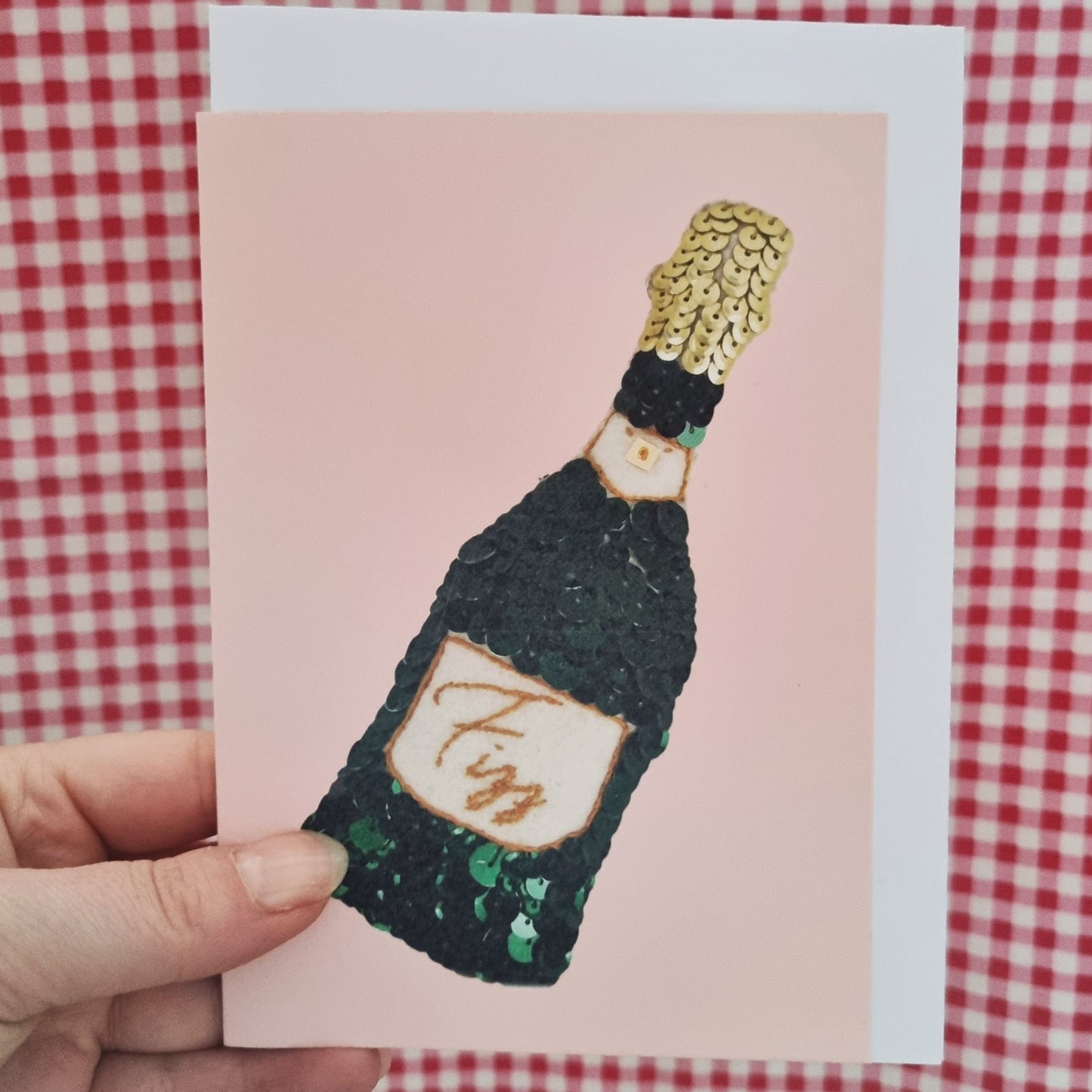 Kate's hand holding a pale pink card with the image of a sequin fizz ornament on it