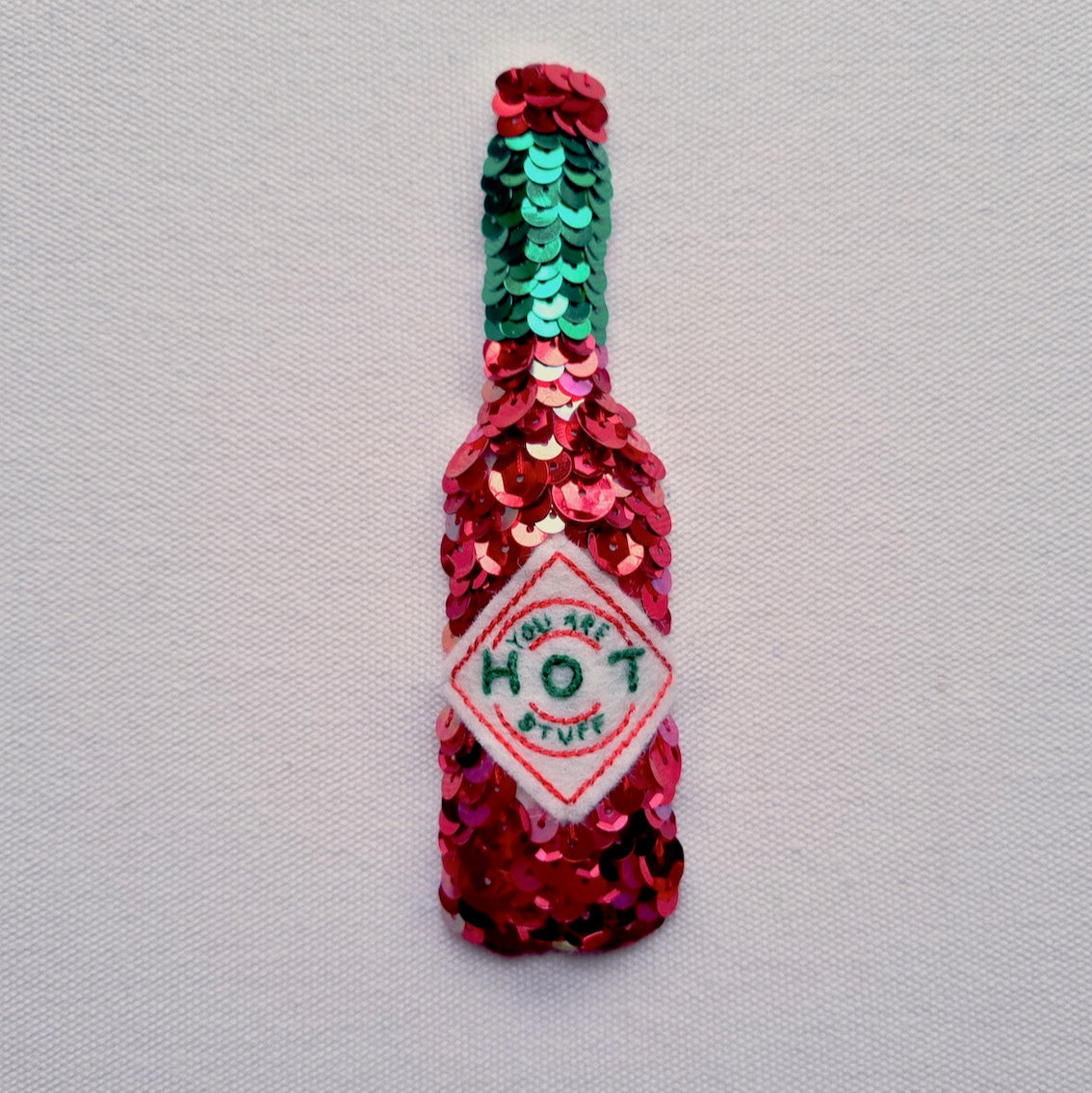 A high quality, artist quality print of a sequinned tabasco bottle that says you are hot stuff on the label