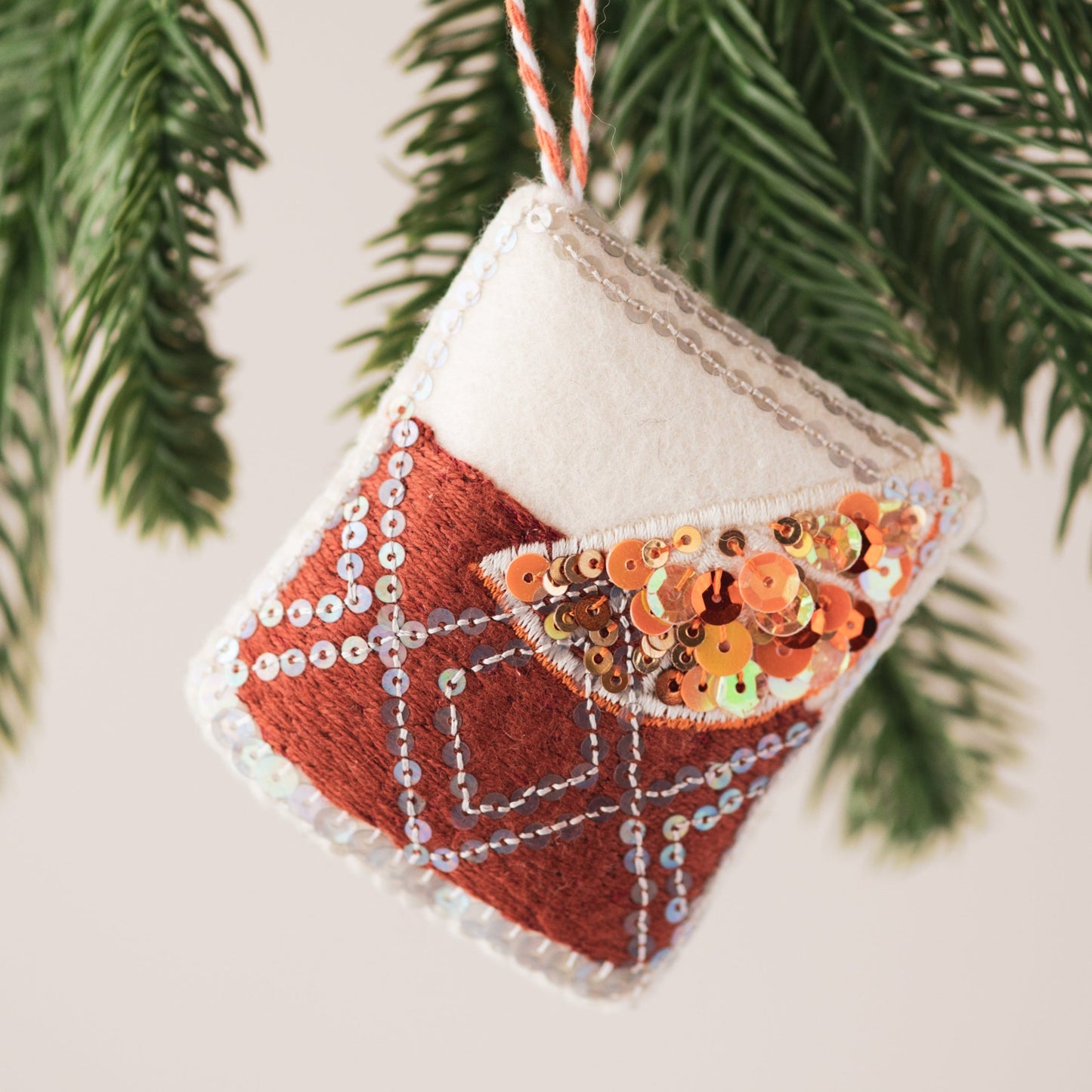 Negroni Sequin Ornament, a sequin and embroidered ornament hanging from a tree branch
