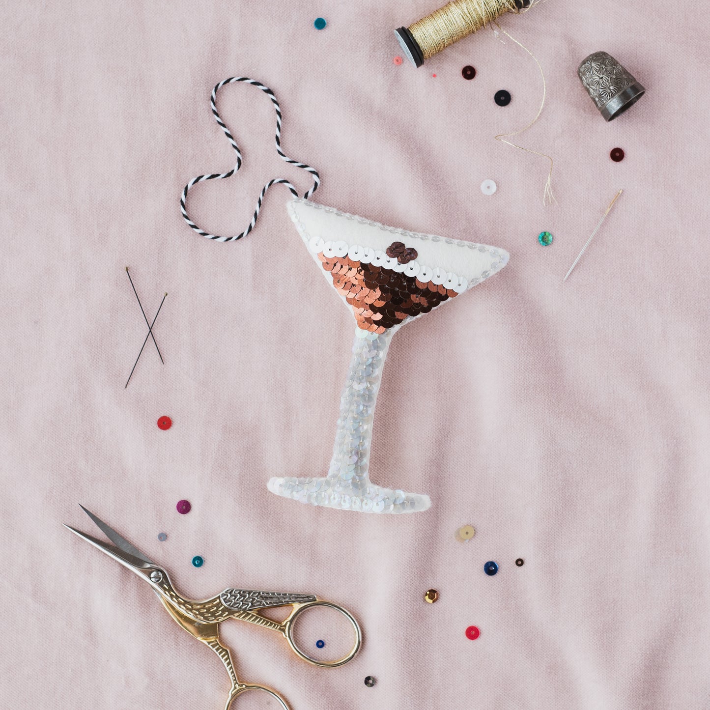 The Espresso Martini Sequin Ornament on a pink background with sequins scattered around