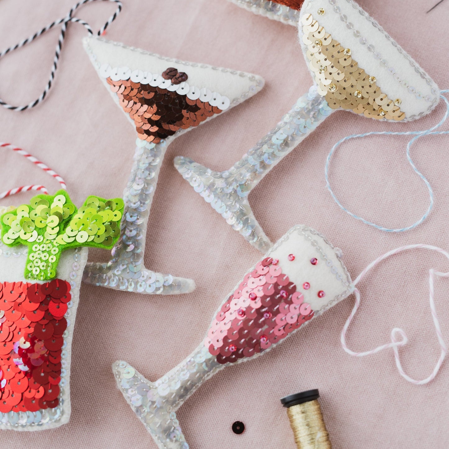 A selection of cocktail glass sequin ornaments on a pink background