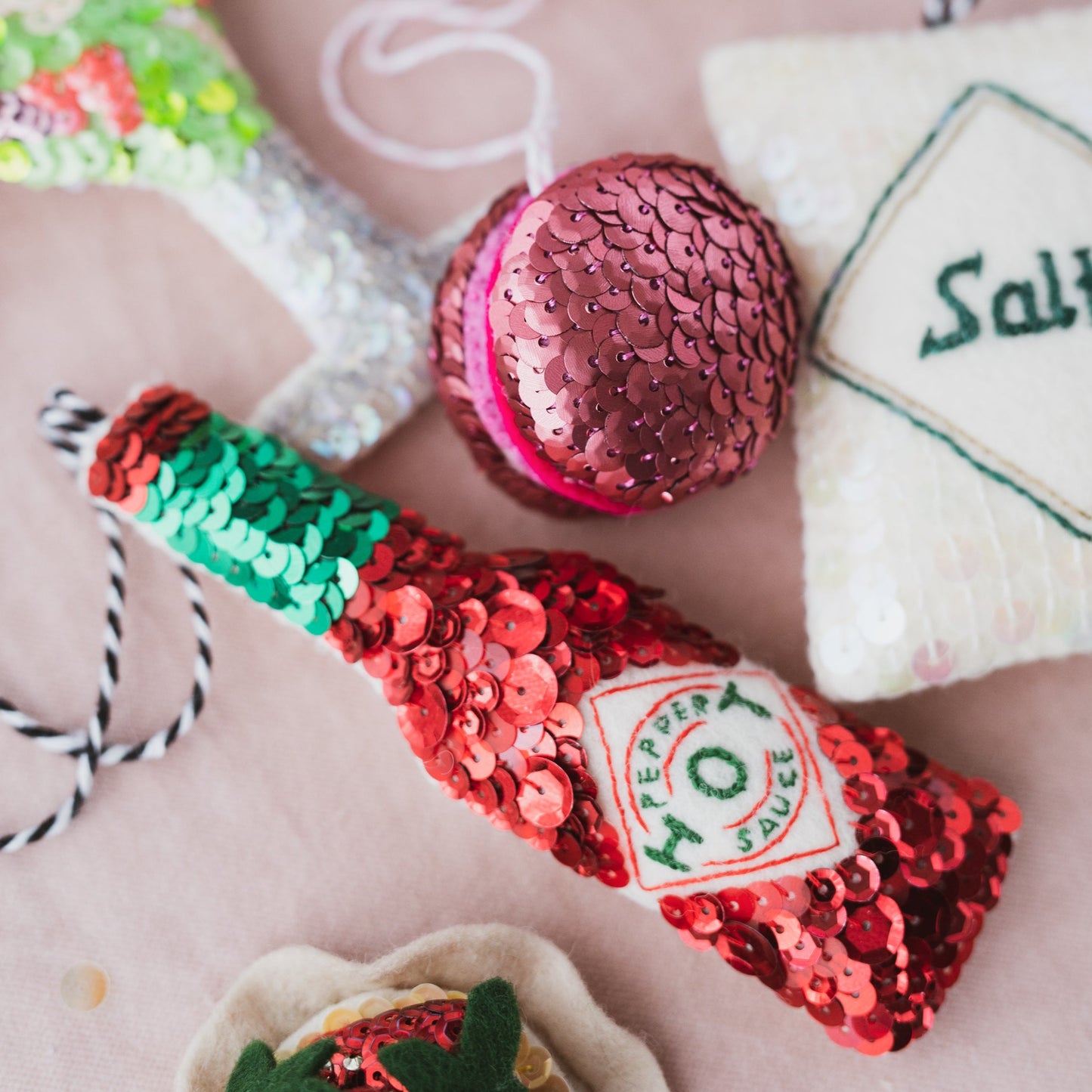 A sequinned tabasco sauce bottle surrounded by other sequin ornaments