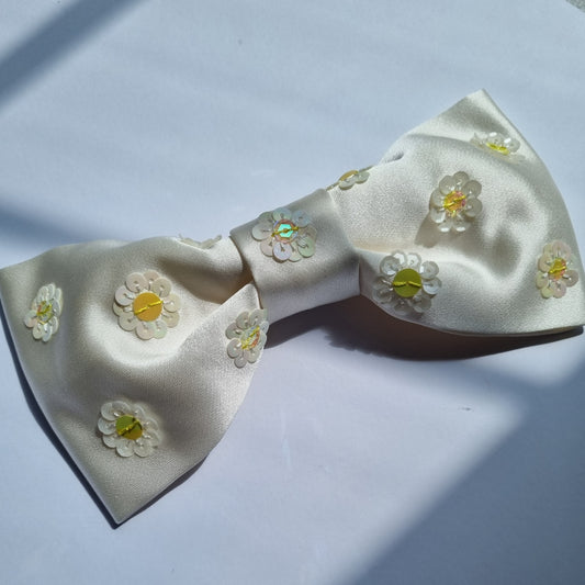 A white silk bow with yellow daisies in sequins embroidered on it
