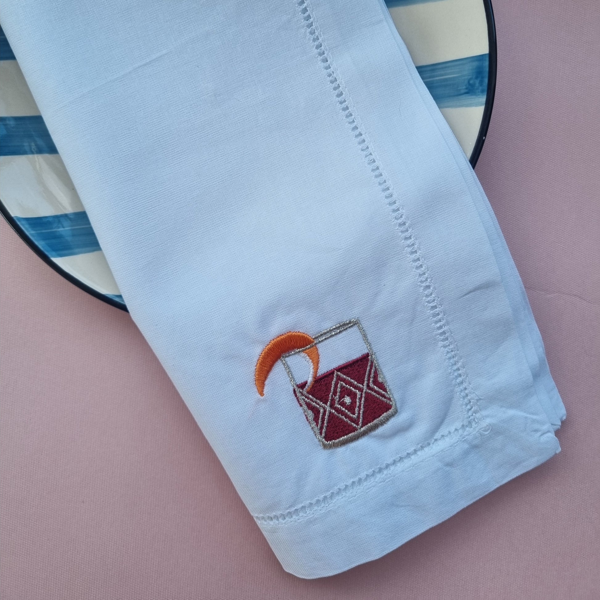 White napkin with an embroidered negroni cocktail.