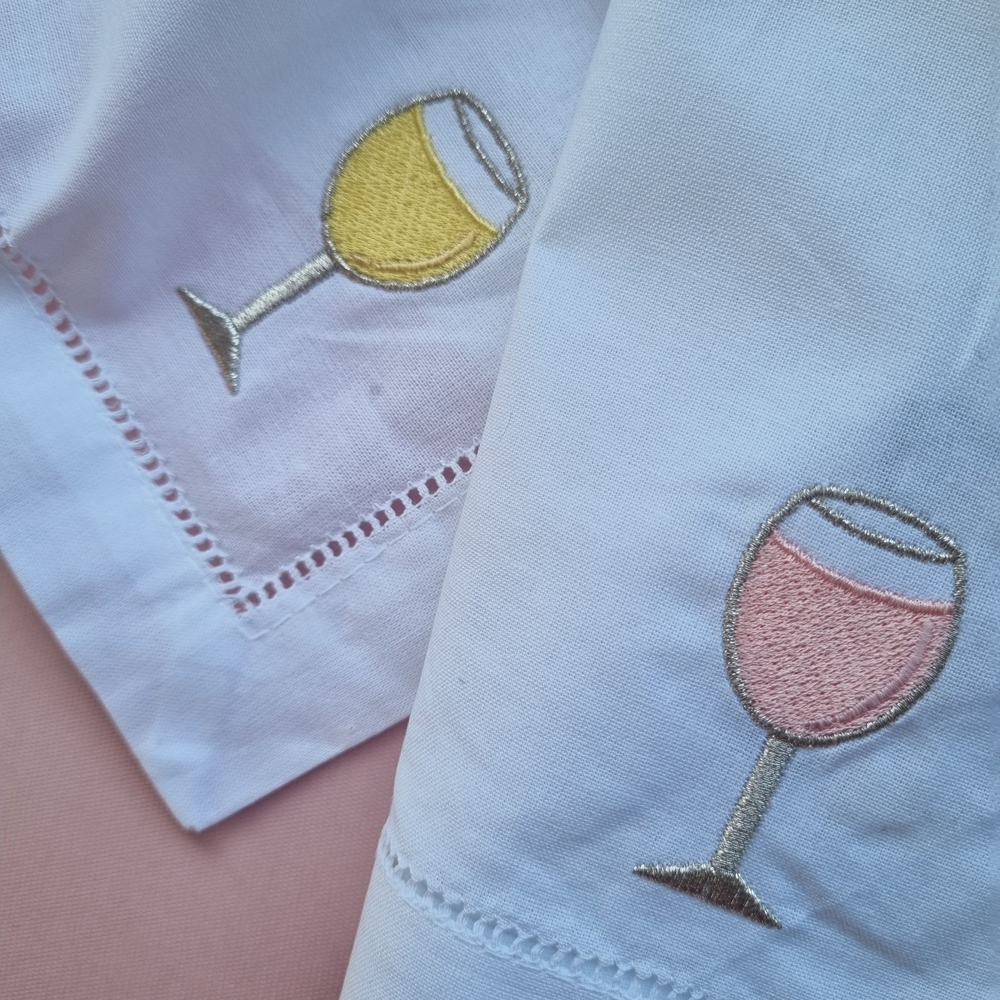 White napkins with embroidered wine glass designs on a pink surface