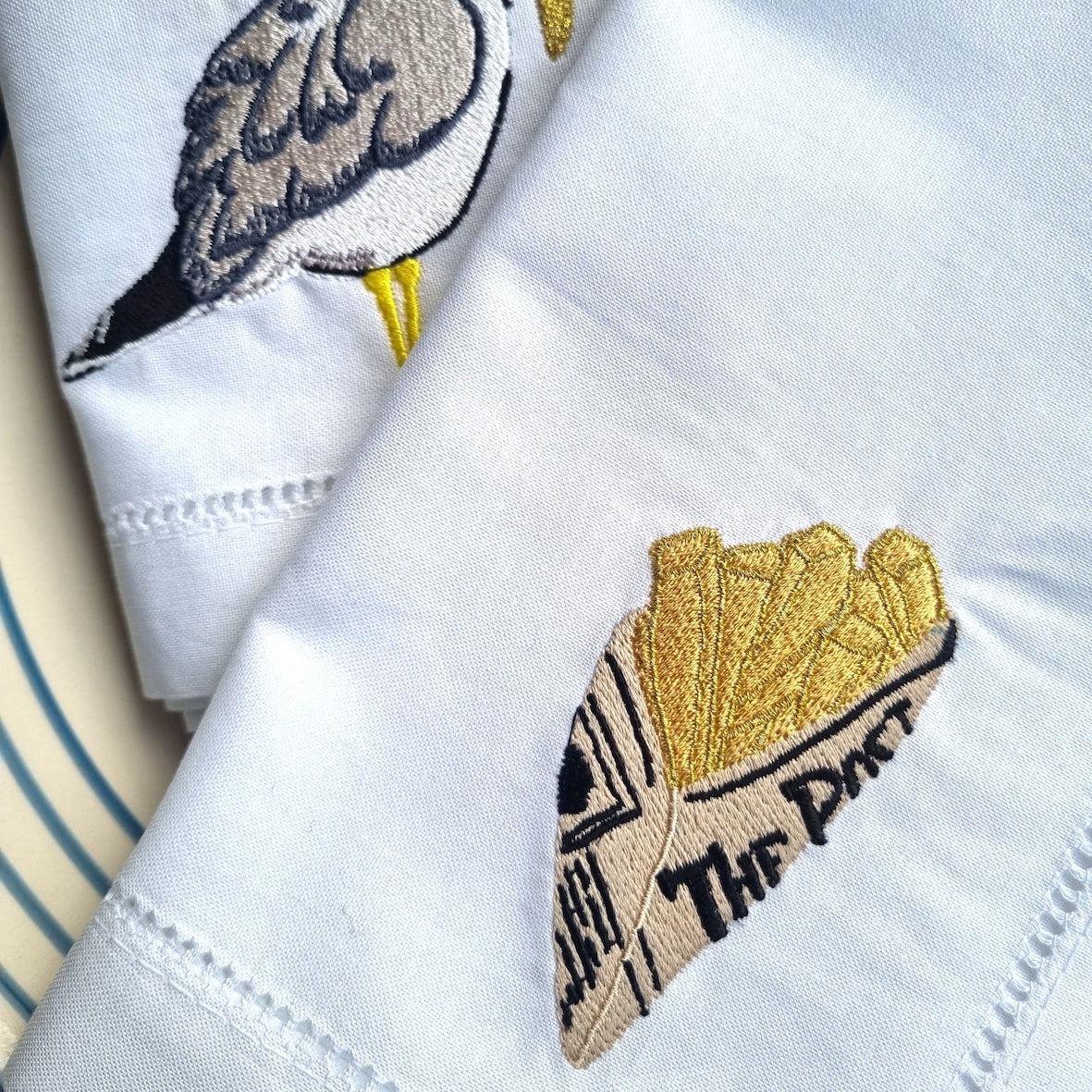 White fabric with embroidered seagull and newspaper cone of chips design