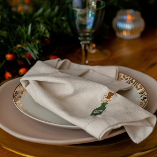 an embroidered champagne bottle napkin on a golden plate