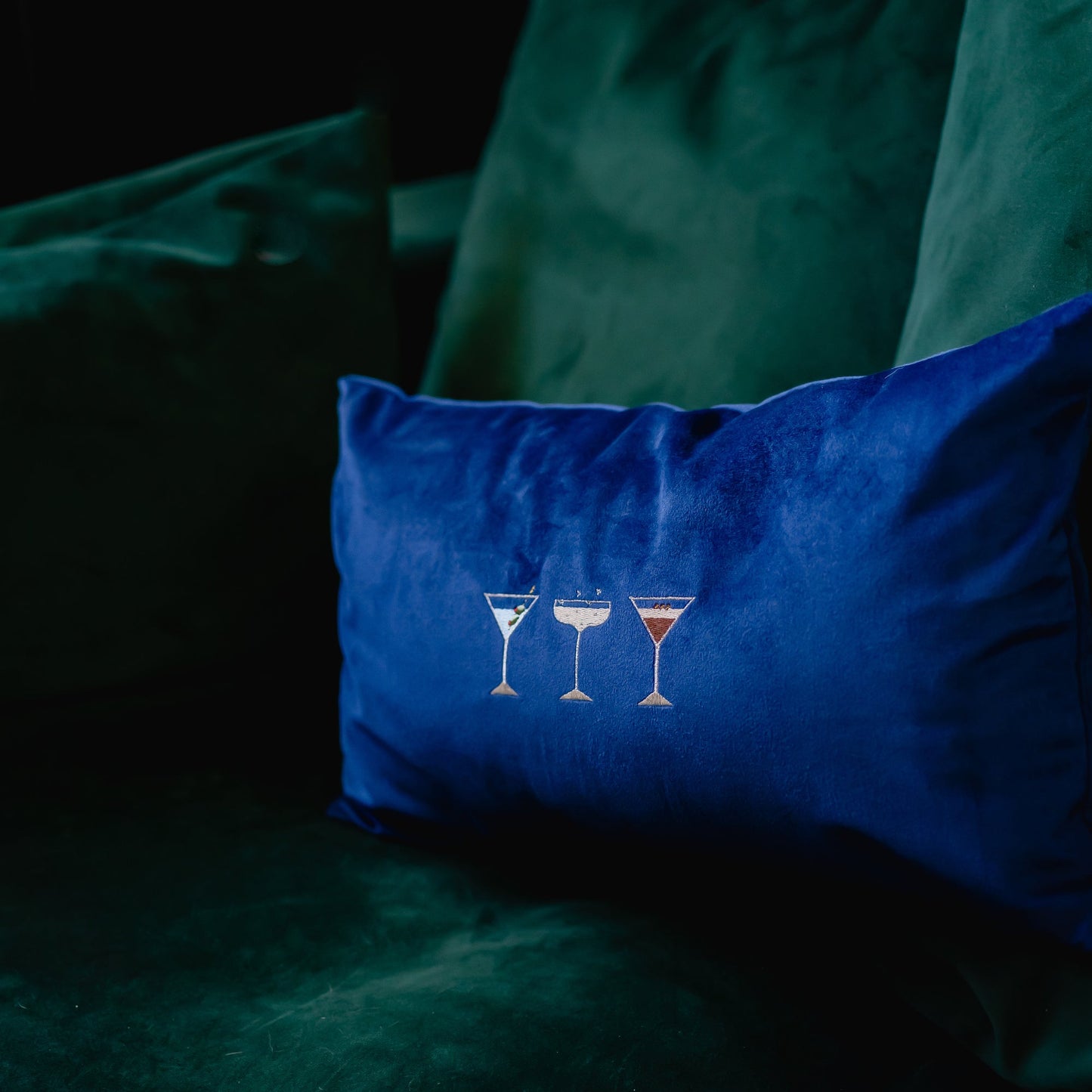 Martini, champagne and espresso martini motifs embroidered on to a navy velvet cushion by Kate Gwilliam