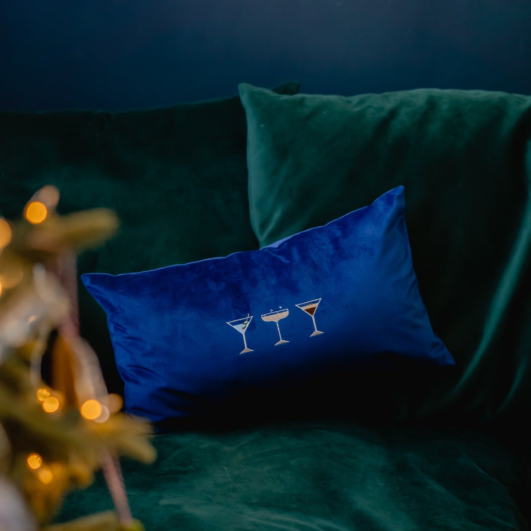 a navy velvet cushion with a martini, champagne, espresso martini embroidered motifs by Kate Gwilliam