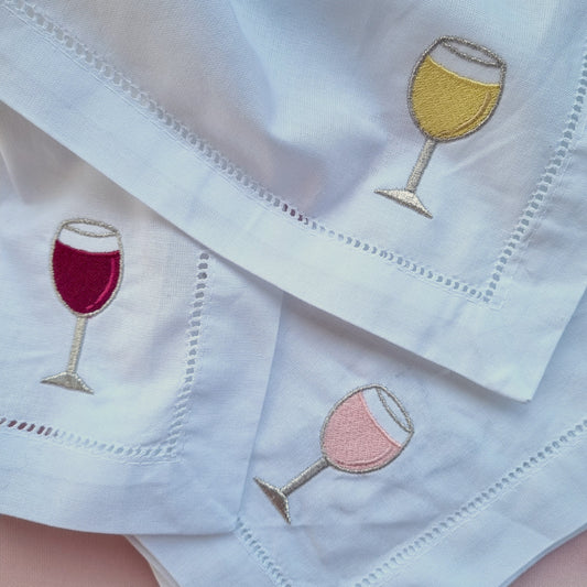 White napkins with embroidered wine glass designs on a light pink background