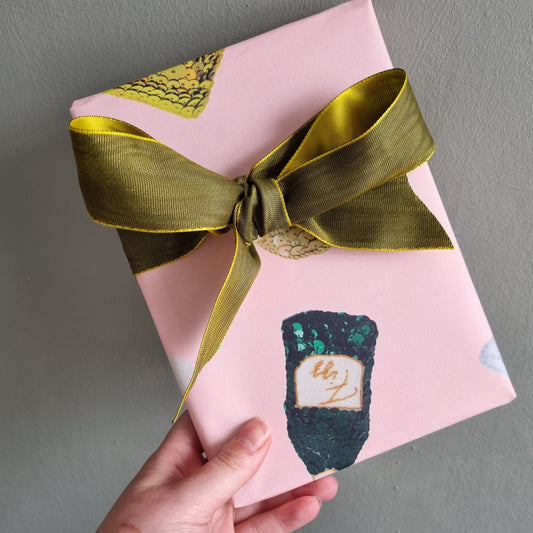 Kate's hand holding a package with her pink printed wrapping paper on it