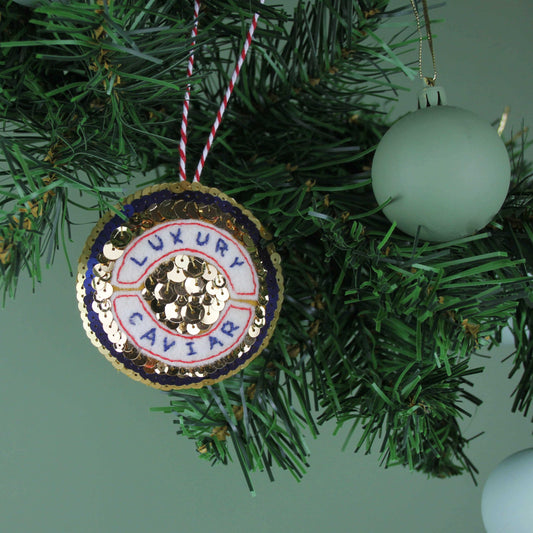 Caviar Decoration, sequinned golden caviar tin ornament hanging on a green tree