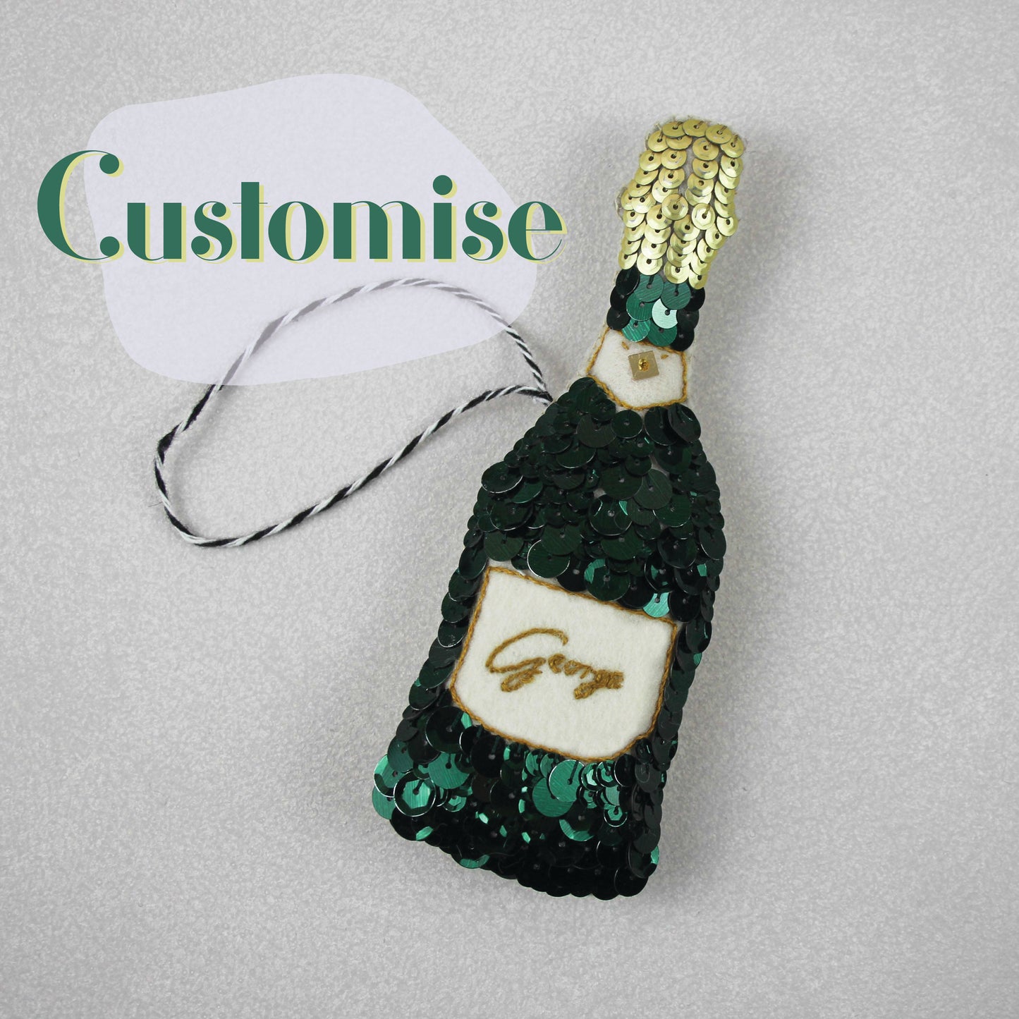 A green sequinned champagne bottle with the name George on the label. In the corner there is a sign saying Customise