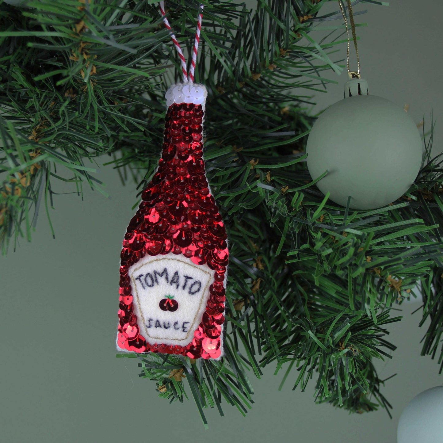 Ketchup Sequin Hanging Ornament, a red sequin ketchup bottle hanging on a green tree