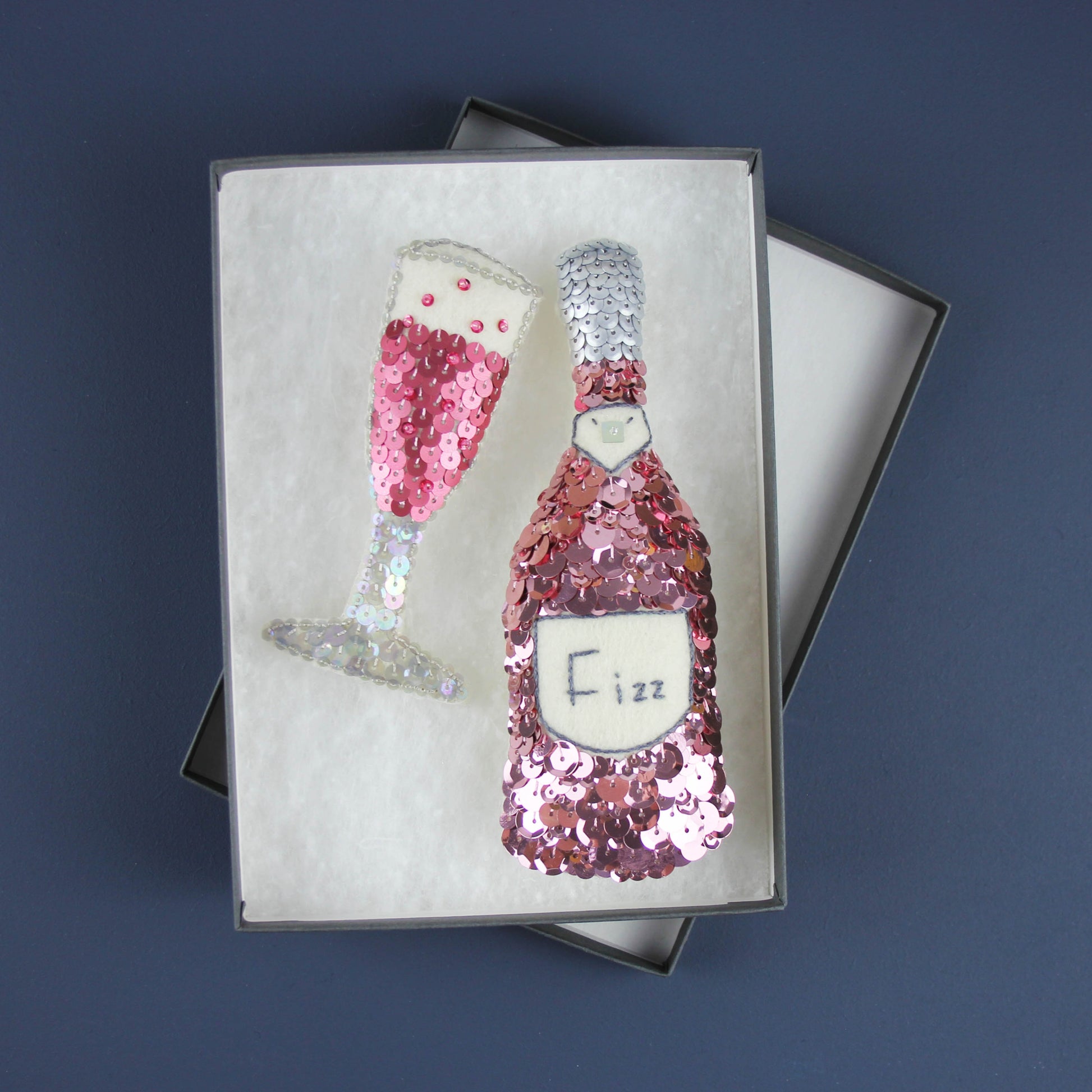 Pink Fizz Sequin Ornament Set, a pink sequinned fizz bottle and a rose pink sequinned champagne flute ornament in a gift box