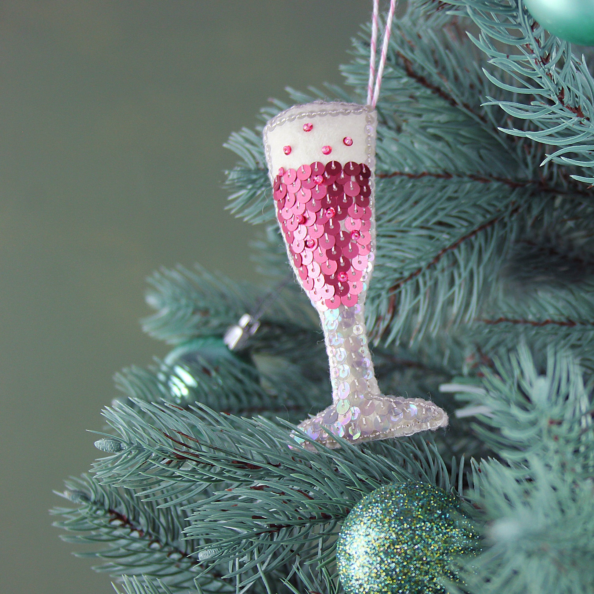 Pink rose champagne flute sequin ornament hanging on a green tree